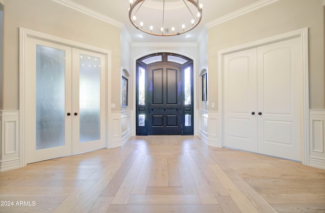 entrance foyer featuring light wood-type flooring, crown molding, an inviting chandelier, and french doors