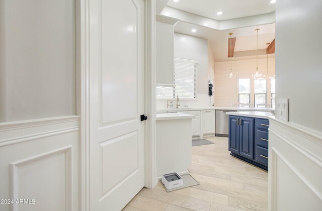 kitchen with an inviting chandelier, blue cabinets, sink, white cabinetry, and light wood-type flooring