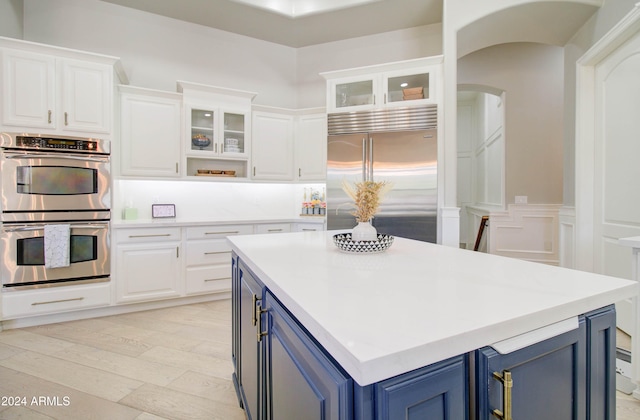 kitchen with stainless steel appliances, blue cabinetry, white cabinetry, and light hardwood / wood-style floors