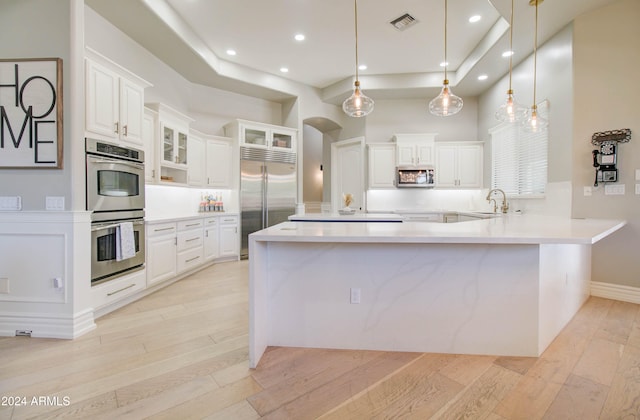 kitchen featuring white cabinets, light wood-type flooring, stainless steel appliances, and hanging light fixtures