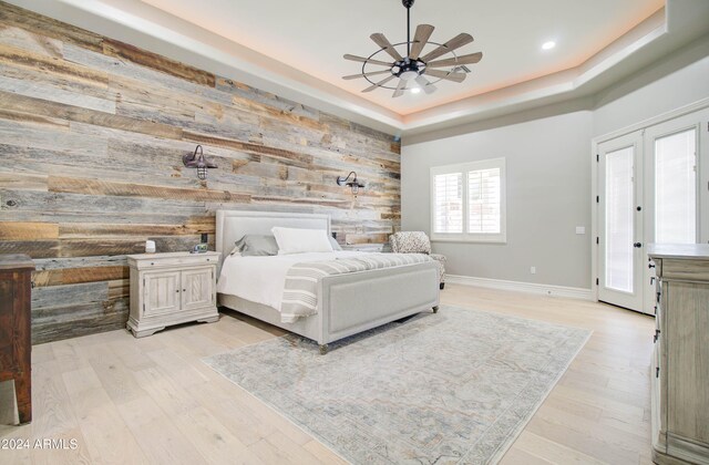 bedroom featuring light hardwood / wood-style floors, wooden walls, a raised ceiling, and french doors