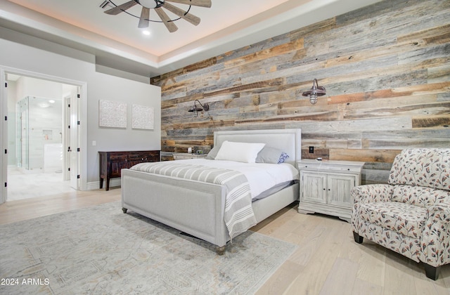 bedroom with wood walls, ensuite bathroom, ceiling fan, and light wood-type flooring