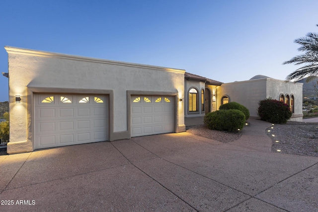 pueblo-style home with driveway, an attached garage, and stucco siding