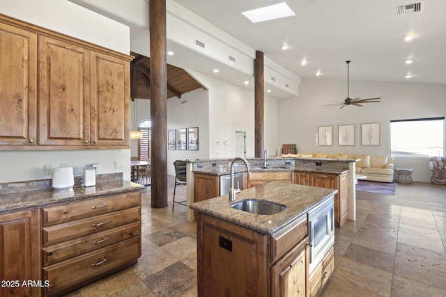 kitchen with stone tile floors, visible vents, a sink, an island with sink, and dark stone counters