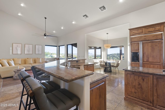 kitchen with paneled built in refrigerator, a breakfast bar area, a sink, and visible vents