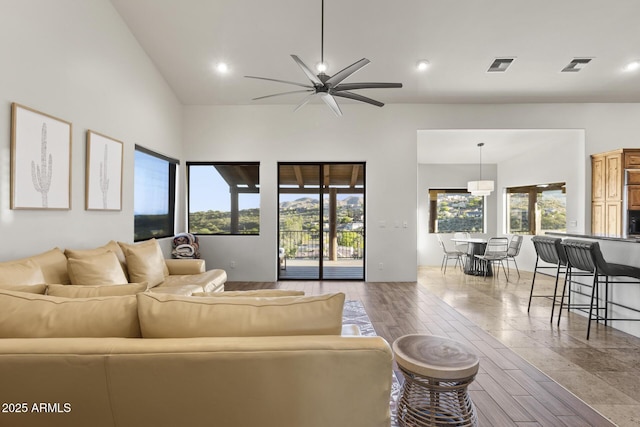 living area with a towering ceiling, wood finished floors, visible vents, and a ceiling fan