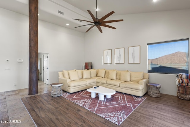 living room featuring visible vents, a towering ceiling, ceiling fan, wood finished floors, and ornate columns