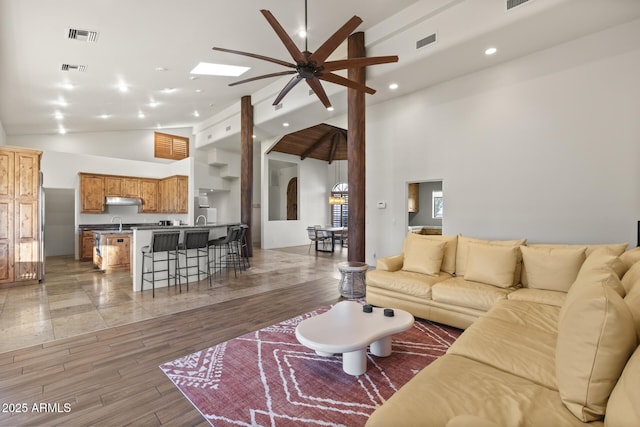 living area featuring high vaulted ceiling, light wood-type flooring, visible vents, and a skylight