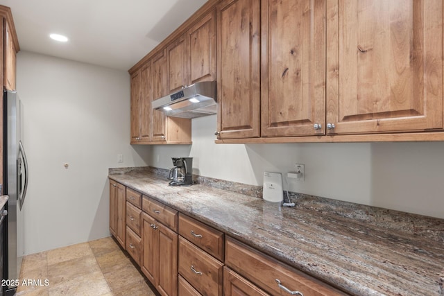 kitchen featuring stone counters, brown cabinets, freestanding refrigerator, and under cabinet range hood