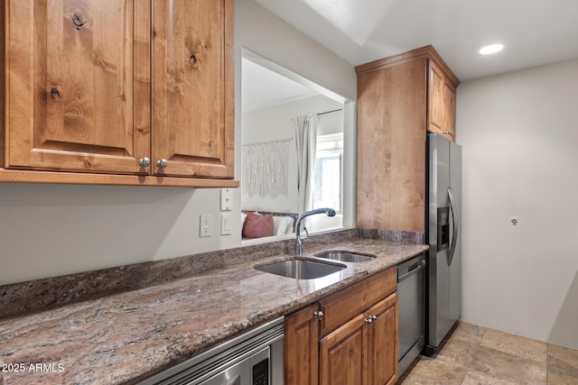 kitchen with stainless steel appliances, brown cabinetry, stone countertops, and a sink