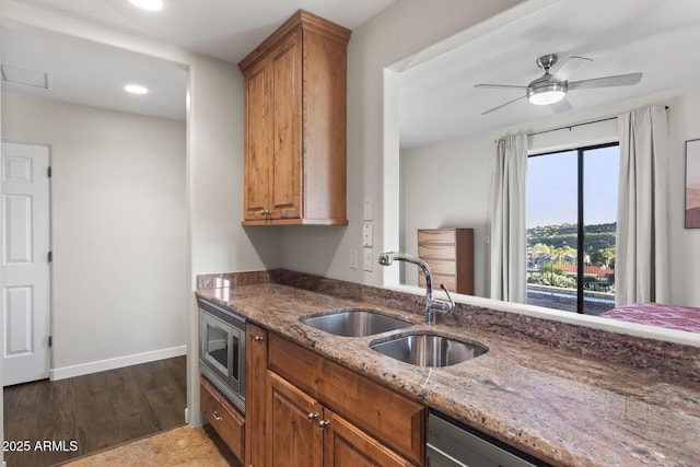 kitchen with light stone counters, brown cabinets, appliances with stainless steel finishes, a sink, and baseboards