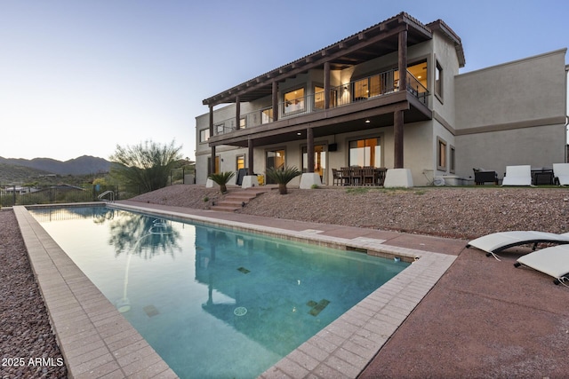 back of property with an outdoor pool, a patio, a balcony, fence, and stucco siding