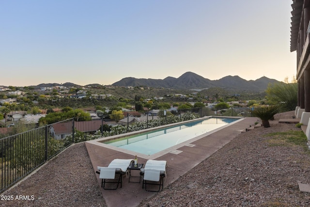 pool at dusk featuring a patio area, fence, a mountain view, and a fenced in pool