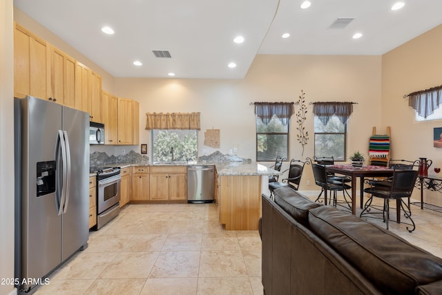 kitchen featuring light brown cabinetry, a peninsula, appliances with stainless steel finishes, and a wealth of natural light