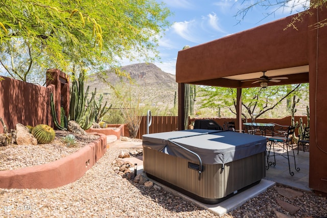 exterior space featuring a hot tub, ceiling fan, fence, and a mountain view