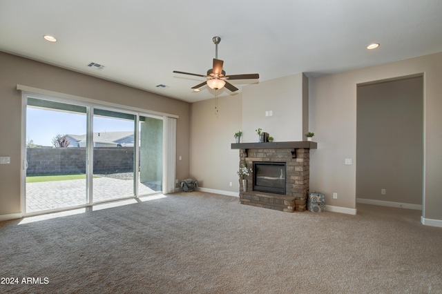 carpeted living room with a stone fireplace and ceiling fan