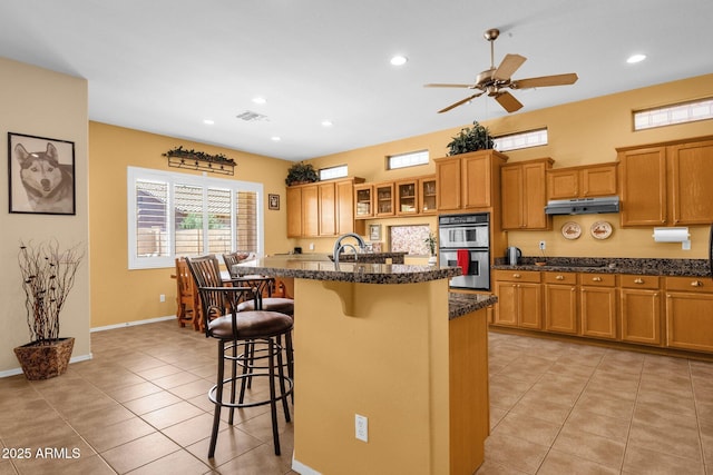 2069 E Winchester Way, Chandler, AZ 85286 - kitchen featuring double oven, brown cabinets, a kitchen bar, light tile patterned floors, and recessed lighting