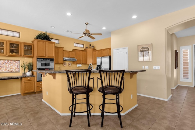 2069 E Winchester Way, Chandler, AZ 85286 - kitchen with appliances with stainless steel finishes, a kitchen bar, under cabinet range hood, ceiling fan, and a center island with sink