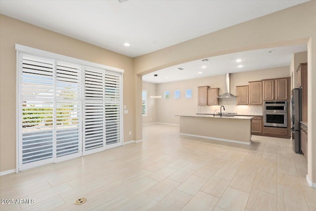 kitchen with open floor plan, wall chimney range hood, appliances with stainless steel finishes, backsplash, and a center island with sink