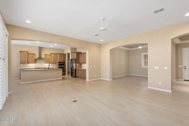 unfurnished living room featuring arched walkways, visible vents, a ceiling fan, and baseboards