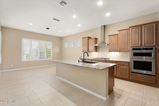 kitchen featuring wall chimney exhaust hood, a sink, a center island with sink, and stainless steel appliances