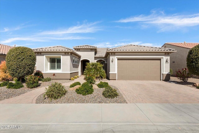 mediterranean / spanish-style home featuring a garage, a tile roof, decorative driveway, and stucco siding