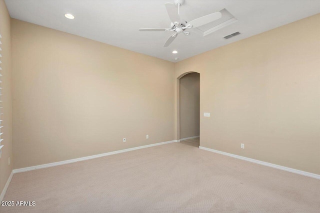 empty room with arched walkways, visible vents, a ceiling fan, light carpet, and baseboards