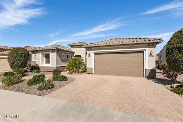 mediterranean / spanish house featuring decorative driveway, a tile roof, an attached garage, and stucco siding