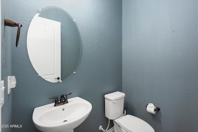 half bath with a textured wall, a sink, and toilet