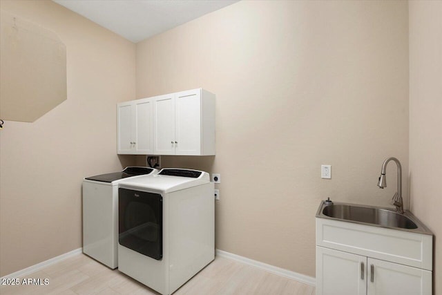 washroom featuring independent washer and dryer, cabinet space, a sink, and baseboards