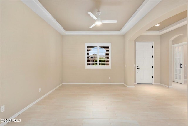 empty room with arched walkways, a raised ceiling, a ceiling fan, and baseboards