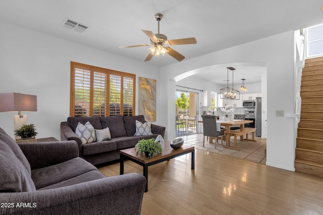 2545 E Harrison Ct, Gilbert, AZ 85295 - living room featuring arched walkways, stairway, ceiling fan, light wood finished floors, and a chandelier
