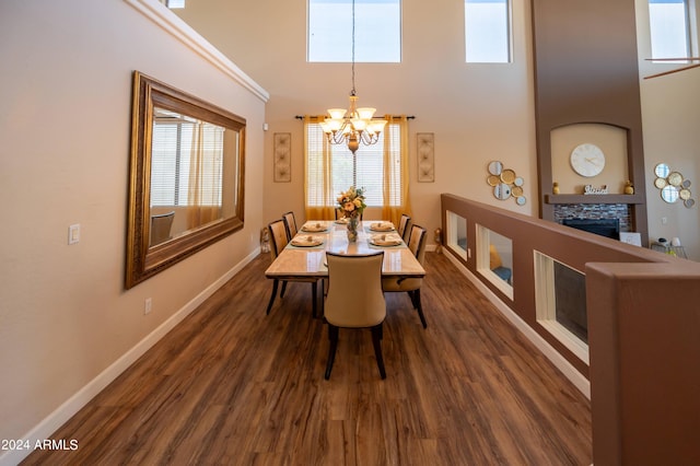 dining area with a towering ceiling, an inviting chandelier, a tiled fireplace, and dark hardwood / wood-style flooring