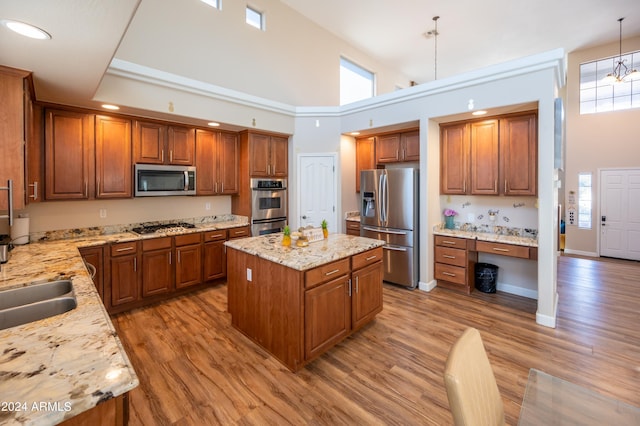 kitchen with a center island, hanging light fixtures, stainless steel appliances, high vaulted ceiling, and light hardwood / wood-style flooring