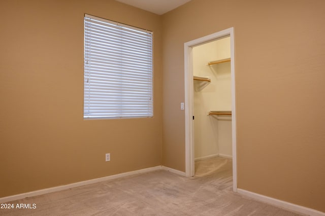 unfurnished bedroom featuring a spacious closet, a closet, and light colored carpet