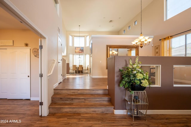 staircase featuring a notable chandelier, wood-type flooring, a towering ceiling, and plenty of natural light