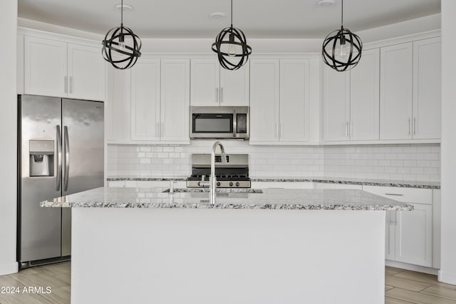 kitchen with white cabinets, appliances with stainless steel finishes, a center island with sink, and decorative light fixtures