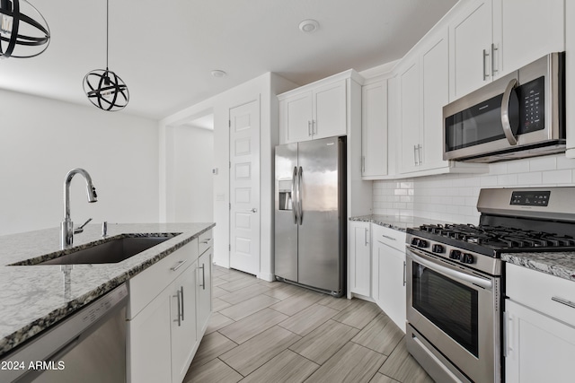 kitchen featuring light stone countertops, appliances with stainless steel finishes, sink, decorative light fixtures, and white cabinetry