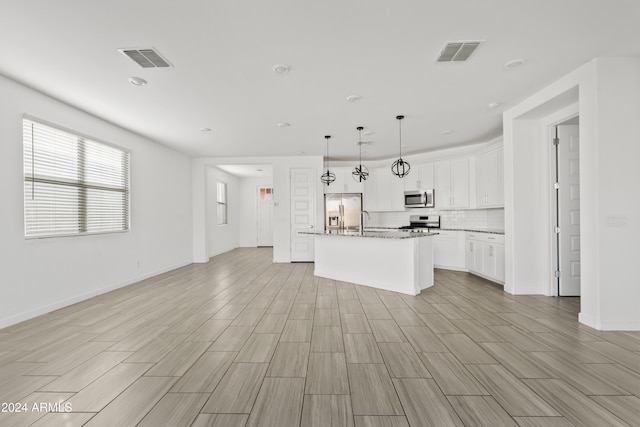 kitchen featuring light stone countertops, an island with sink, decorative light fixtures, white cabinetry, and stainless steel appliances