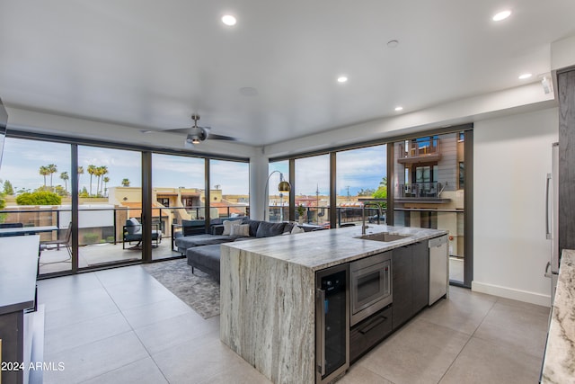 kitchen with a kitchen island with sink, stainless steel appliances, ceiling fan, light stone counters, and light tile patterned flooring