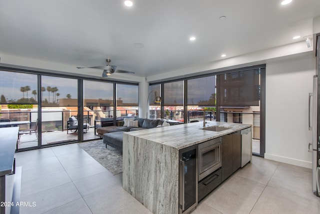 kitchen featuring light stone countertops, a center island with sink, light tile patterned floors, sink, and ceiling fan