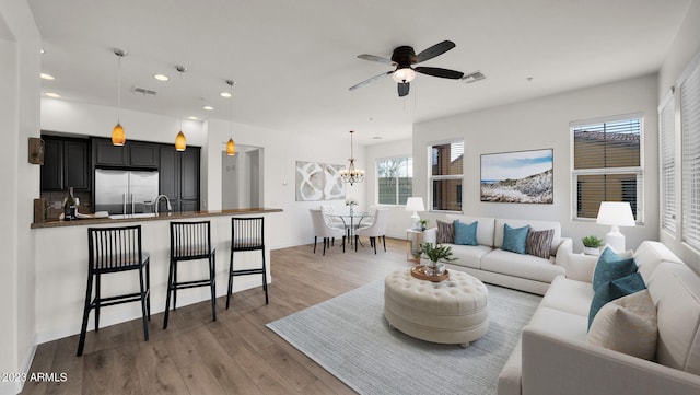 living room featuring sink, light hardwood / wood-style floors, and ceiling fan with notable chandelier