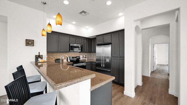 kitchen with appliances with stainless steel finishes, decorative light fixtures, decorative backsplash, dark hardwood / wood-style floors, and kitchen peninsula