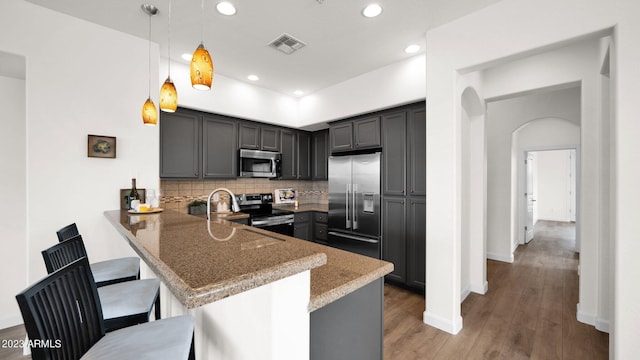 kitchen with a kitchen breakfast bar, wood finished floors, a peninsula, stainless steel appliances, and backsplash