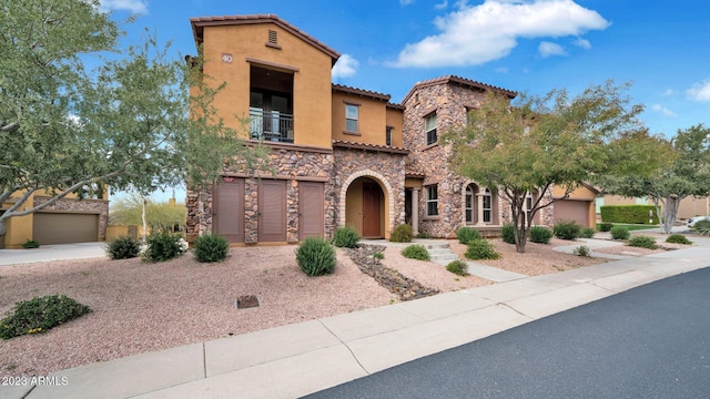 mediterranean / spanish-style house with an attached garage, a balcony, a tile roof, stone siding, and stucco siding