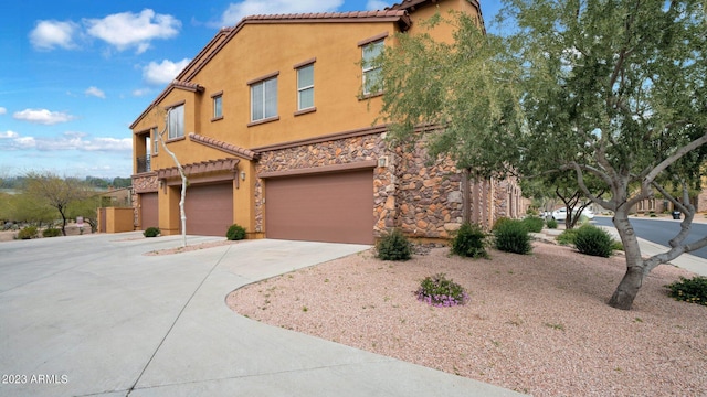 view of front facade featuring a tile roof, stucco siding, concrete driveway, an attached garage, and stone siding