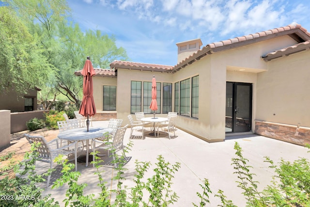 back of property featuring outdoor dining space, a patio area, a tiled roof, and stucco siding