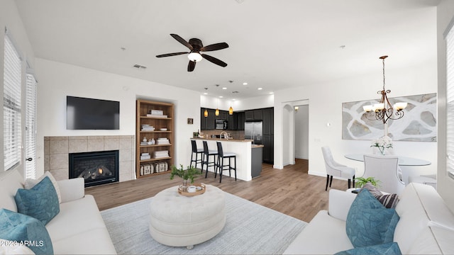 living room featuring light hardwood / wood-style floors, ceiling fan with notable chandelier, and a tiled fireplace