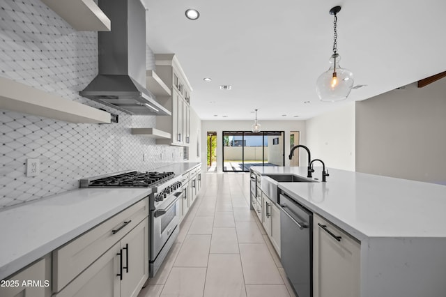 kitchen featuring a sink, decorative backsplash, hanging light fixtures, appliances with stainless steel finishes, and wall chimney exhaust hood