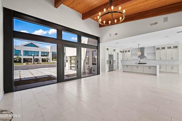 unfurnished living room with visible vents, plenty of natural light, wooden ceiling, beamed ceiling, and a chandelier